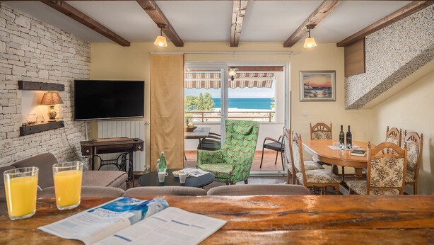 A cozy living area with a television, a wooden table with drinks, and a view of the sea through a glass door. - New and modern stylish apartment with 3 bedrooms in one of the best locations in Porec, close to the beach and with sea view (Porec)