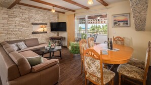 A cozy living room with a stone wall, a flat-screen TV, a wooden dining table with chairs, and a view of the outdoors. - New and modern stylish apartment with 3 bedrooms in one of the best locations in Porec, close to the beach and with sea view (Porec)
