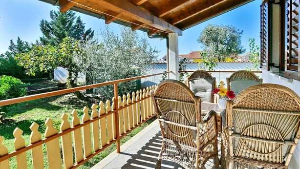 Un espacio al aire libre techado con sillas de mimbre y una mesa, con vistas a un jardín y una zona residencial.
