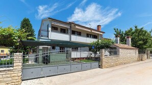 Ein zweistöckiges Haus mit Balkon, überdachter Terrasse und Steinmauer.