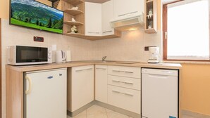 Eine kleine Küche mit weißen Schränken, einer Mikrowelle, einem Kühlschrank und einer Kaffeemaschine.