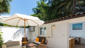 An outdoor patio with wicker furniture, a white umbrella, and a cityscape painting on the wall. - Charming Bungalow with a Terrace - Pet Friendly (Porec)