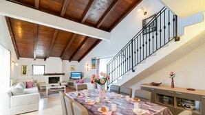 Un vaste espace de vie doté d’un haut plafond, une table à manger dressée pour le repas et un escalier menant à l’étage supérieur.