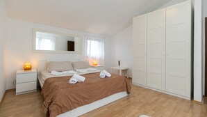 Une chambre à coucher comprenant un lit, des tables de chevet, une commode, un miroir, une armoire et une fenêtre avec des rideaux.