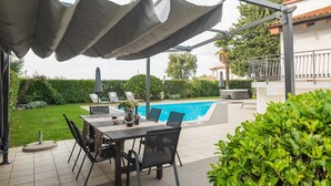 Une terrasse extérieure avec une piscine, une table et des chaises, ainsi qu’un espace abrité.