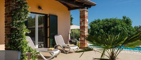 Un patio con dos sillones de descanso, una planta en maceta y una piscina.