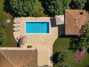Vista aérea de una propiedad con piscina, sillas de descanso y un patio cubierto.
