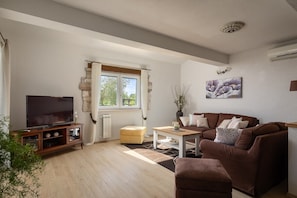 Ein Wohnzimmer mit Fernseher, Sofa, Couchtisch und einem fensterbepflanzten Fenster.
