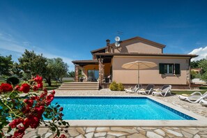 Une maison à deux étages avec une piscine, un espace salon extérieur et un jardin.