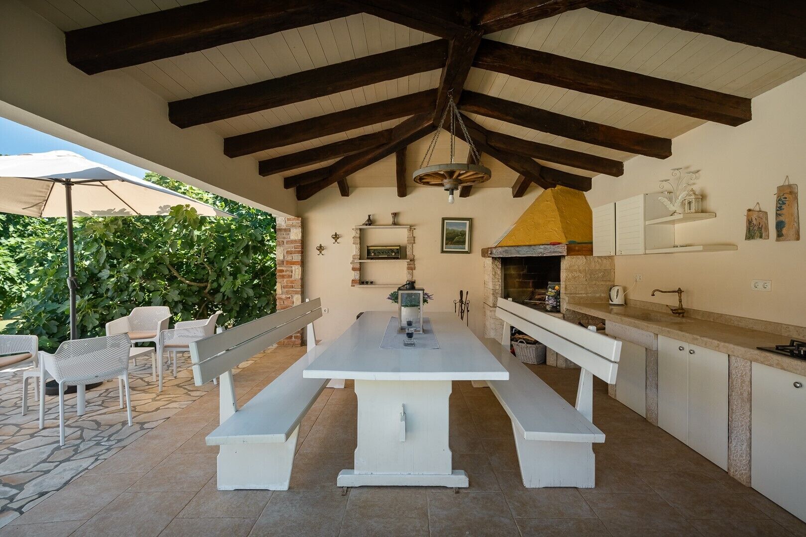Un espace cuisine extérieur avec une longue table blanche, des bancs et un four à pizza.