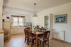 Un comedor con una mesa y sillas de madera, una cocina al fondo y un cuadro en la pared.