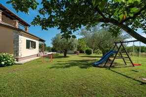 Una propiedad residencial con jardín césped, área de juegos con tobogán y una casa de fachada de piedra y ladrillo.