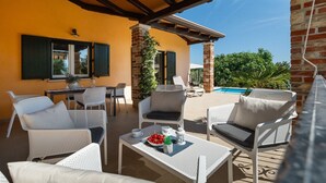 An outdoor patio with white wicker furniture, a dining table, and a pool in the background.