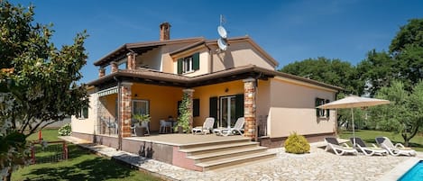 A two-story house with a patio, a swimming pool, and a garden.