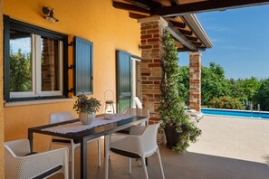 Une terrasse extérieure avec une table et des chaises, un pot de fleurs et une vue sur une piscine.