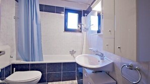 Baño con inodoro, lavabo, ducha y una pequeña ventana.