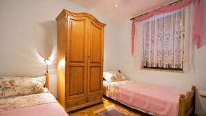 Un dormitorio con dos camas individuales, un armario de madera, una ventana con cortinas de encaje y una lámpara de pie.