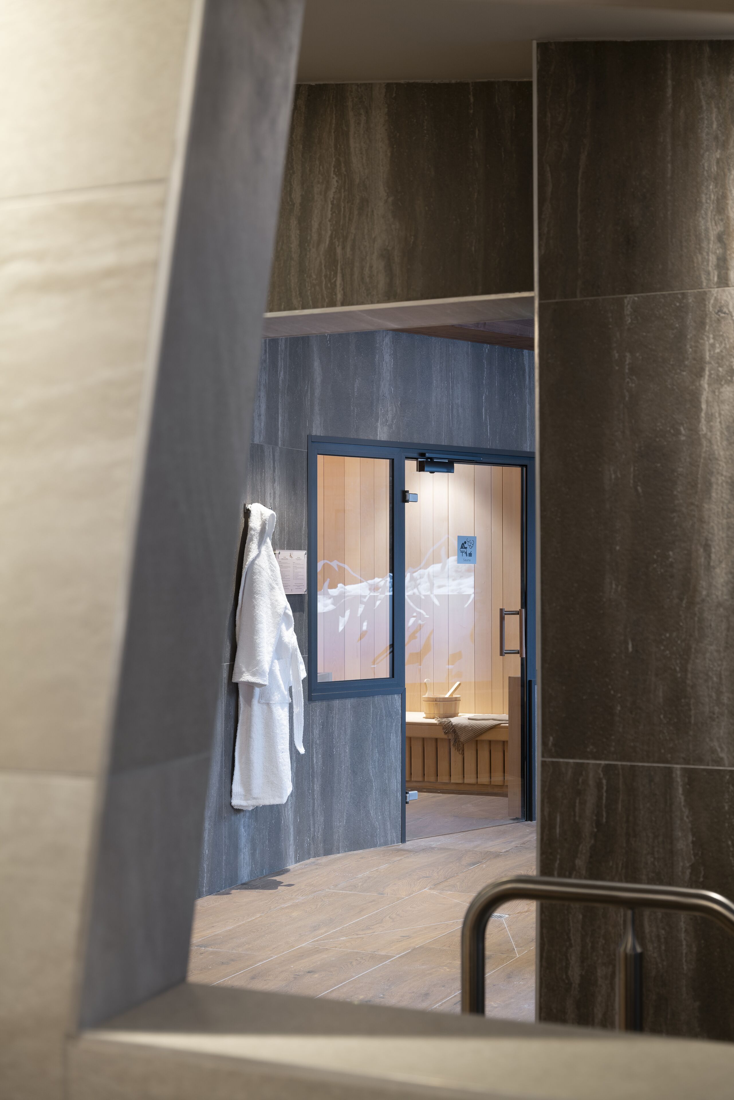 A modern bathroom with a glass door, a towel rack, and a wooden bench.