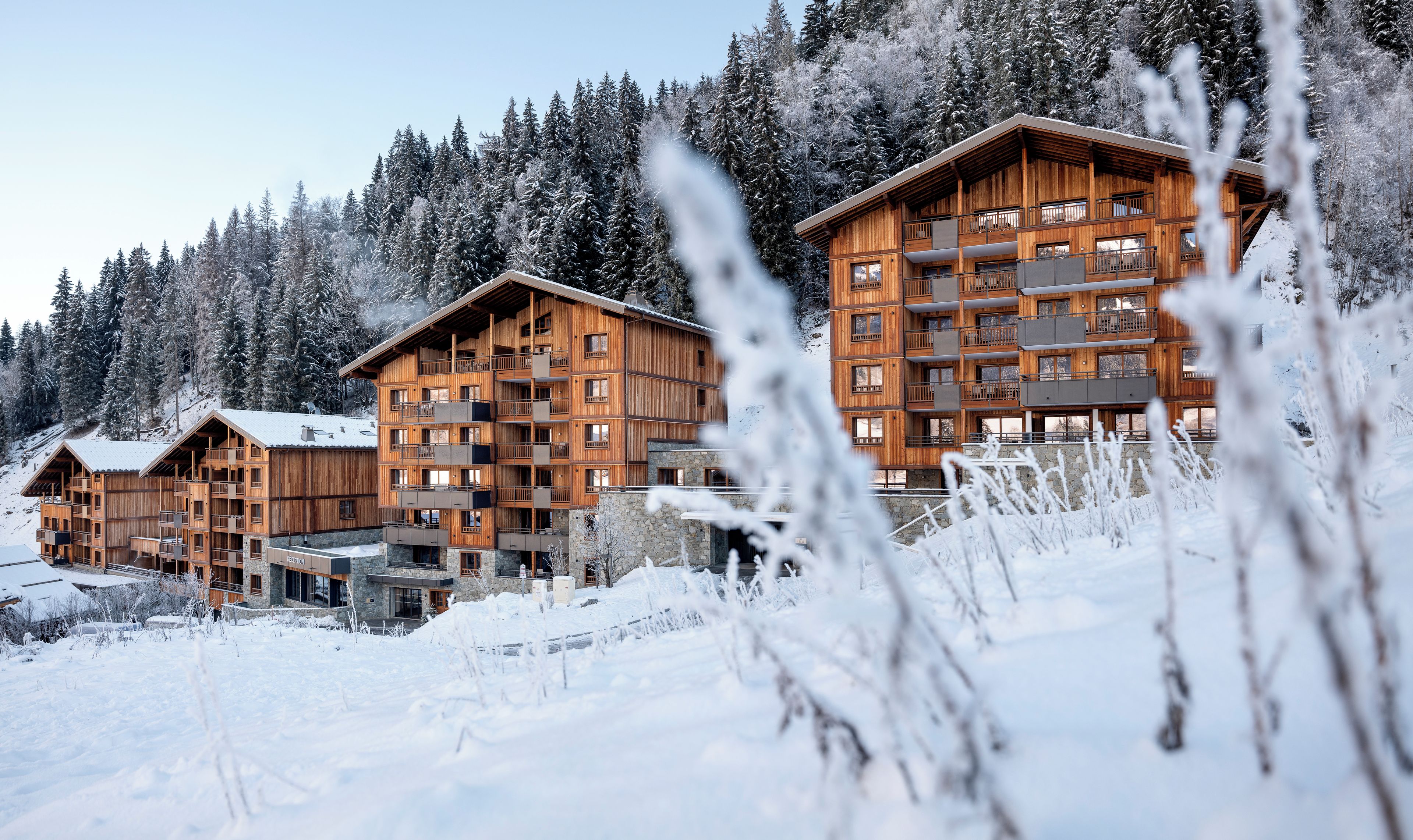 A wooden multi-story building with balconies, surrounded by snow-covered trees.