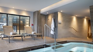 Een moderne spa-ruimte met een glazen hottub, twee loungestoelen en uitzicht op de stad door grote ramen.
