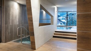 Een modern binnenzwembad met uitzicht op besneeuwde bergen, een trap en een glazen balustrade.