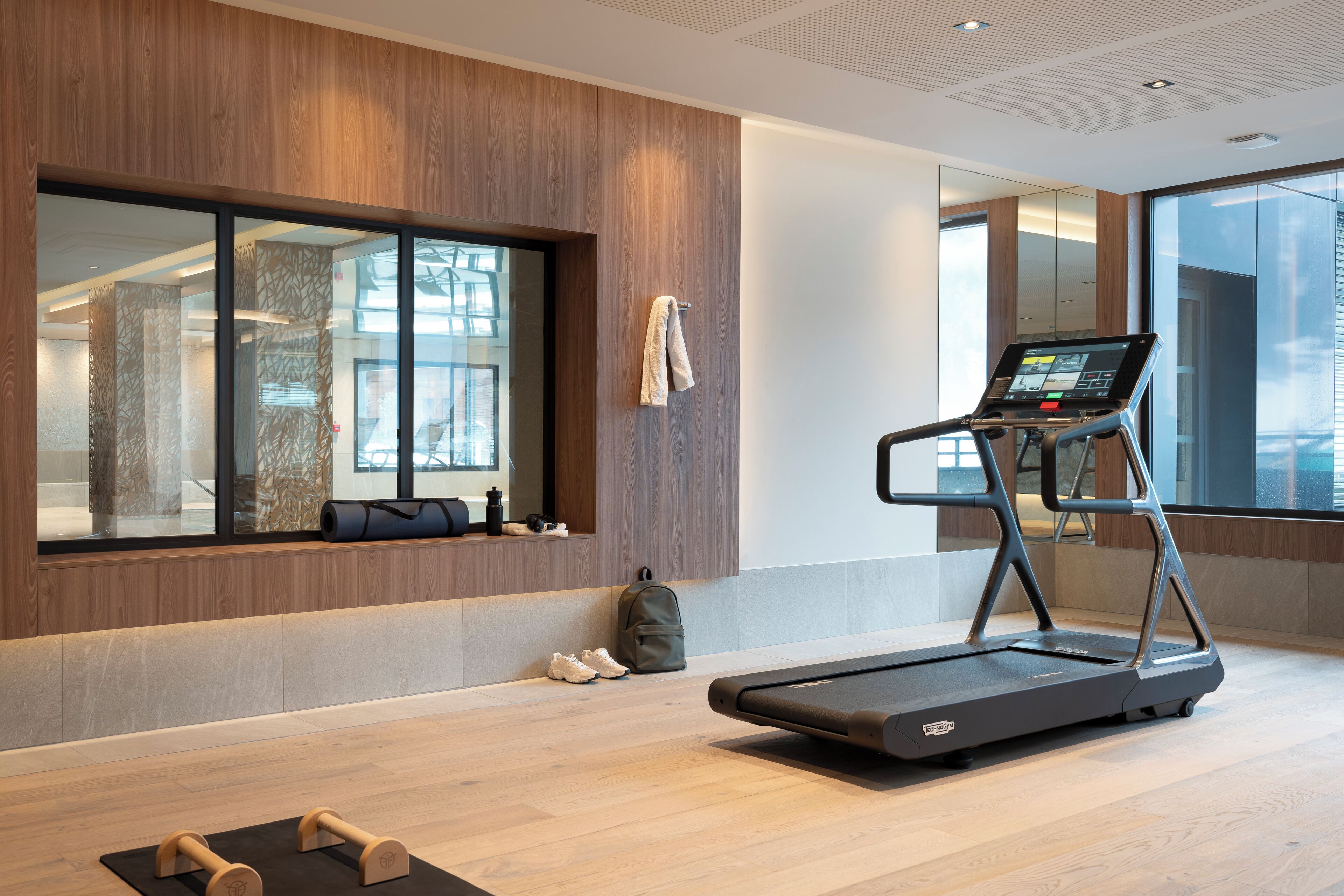 A modern gym with a treadmill, weights, and a large window offering a view of the city.