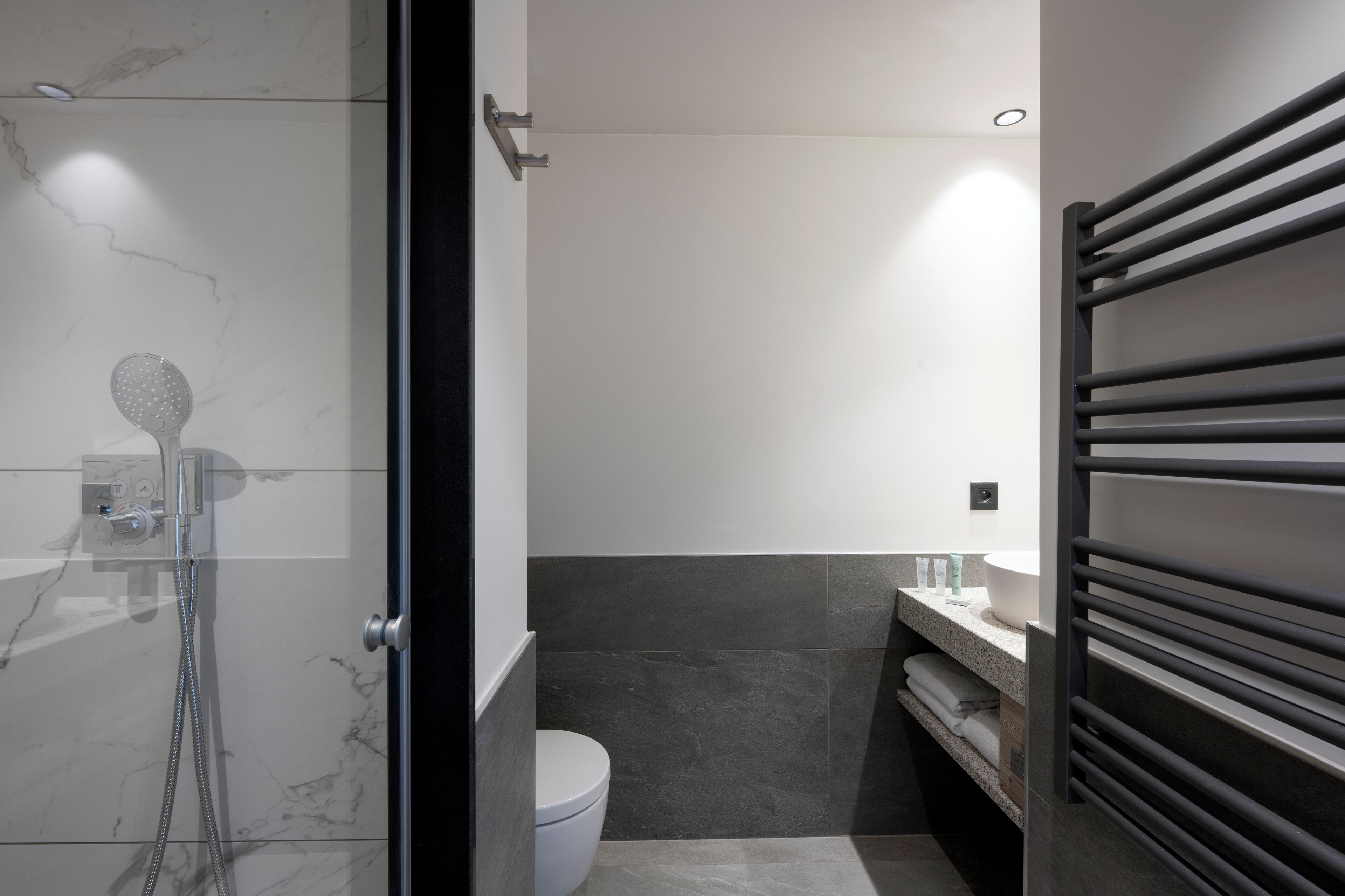 Un baño moderno con ducha de vidrio, inodoro y tocador con toallero.