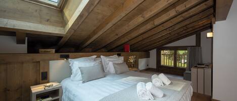 Un dormitorio con tragaluz, vigas de madera, una cama con almohadas, una mesita de noche y un buró.