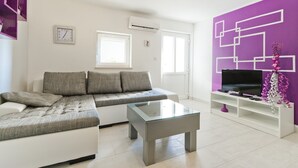 A modern living room with a sofa, a glass coffee table, and a TV on a white stand.