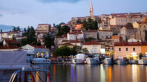 A coastal town with historic buildings, a prominent tower, and a marina with boats.