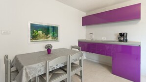 A compact kitchen with a purple countertop, a small sink, and a coffee machine. There is a dining table with chairs and a potted plant on it.