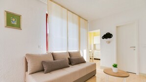 Un soggiorno moderno con un divano beige, un piccolo tavolino con una pianta e una cucina visibile sullo sfondo.