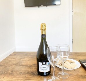 En flaska prosecco, två tomma vinglas och en tallrik med kakor på ett träbord.