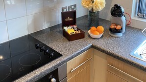 A kitchen with a black stove, wooden cabinets, a stainless steel range hood, and a countertop with a coffee maker, a vase with flowers, and a bowl of oranges. - Tudors eSuites Balcony Apartment (Birmingham)