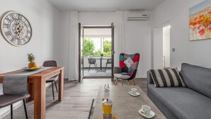 A modern living room with a grey sofa, a patterned armchair, a wooden dining table with a pineapple and a plate, and a large wall clock. - Oroz / Apartment Oroz II (Porec)