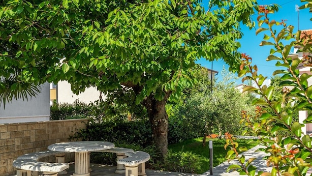 A courtyard with a stone table and benches, surrounded by lush greenery and a tree. - Oroz / Oroz Studio II (Porec)