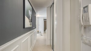 Un pasillo con un teléfono blanco, un cuadro en la pared y una puerta que da a otra habitación.