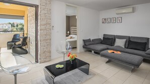Una sala moderna con un sofá gris, una mesa de centro de vidrio y una zona de comedor con sillas.