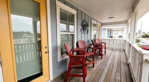 Une véranda couverte avec un plancher en bois, une balustrade blanche et des fauteuils Adirondack rouges.