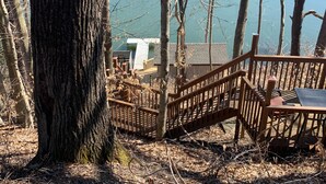 A wooden deck with a bench, overlooking a lake with a building in the background. - Lakefront, family friendly home -Baseball campers! (Oneonta)