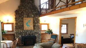 A cozy living room with a stone fireplace, wooden furniture, and a high ceiling with exposed beams. - Lakefront, family friendly home -Baseball campers! (Oneonta)