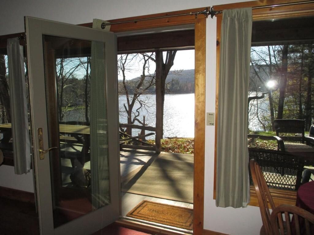 Une pièce dotée d’une porte vitrée donnant sur une terrasse d’où l’on peut admirer un lac et des arbres.