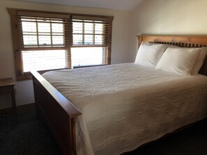 A bedroom with a wooden bed frame, a large window with blinds, and a nightstand. - Lakefront, family friendly home -Baseball campers! (Oneonta)