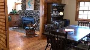A dining area with a wooden table and chairs, a stone wall, and a fireplace. - Lakefront, family friendly home -Baseball campers! (Oneonta)