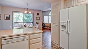 Una cocina con un refrigerador blanco, un comedor con sillas y una ventana que ofrece vistas a árboles.