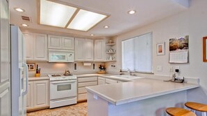 Una cocina moderna con armarios blancos, una isla central con taburetes, horno empotrado y microondas.
