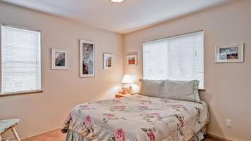 Un dormitorio con colcha estampada, lámpara de noche y cuadros en las paredes.