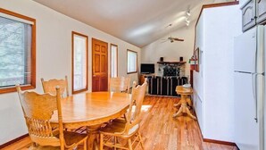 Un coin repas avec une table et des chaises en bois, une cuisine équipée d’un réfrigérateur et d’une cuisinière, et un ventilateur de plafond.