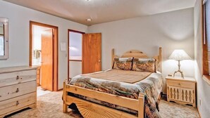 Une chambre à coucher avec un lit en bois, une table de chevet avec une lampe, une commode et une porte donnant sur une autre pièce.