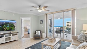 A spacious living room with a television, a sofa, a coffee table, and a view of the ocean through large sliding doors. - Destin West Heron 505 ~ 3BR/2.5BA ~ Bay Views ~ Overlooking the Lazy River (Fort Walton Beach)